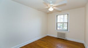 vacant bedroom with hardwood floors, ceiling fan, radiator and window at 4020 Calvert street apartments in washington dc