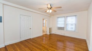 vacant bedroom with hardwood floors, ceiling fan and large windows at hampton courts apartments in washington dc