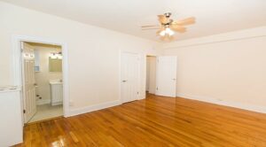 vacant living area with hardwood floors, ceiling fan and view of front entrance and bathroom at the klingle apartments in cleveland park washington dc
