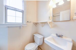 bathroom with toilet, built in shelving, mirror, sink and window at 1818 Riggs place apartments in washington dc