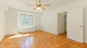 vacant bedroom with wood flooring, large window and ceiling fan at 2800 woodley road apartments in washington dc