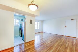 vacant living area with hardwood floors, large window and view of kitchen and front entrance at cambridge square apartments in bethesda maryland