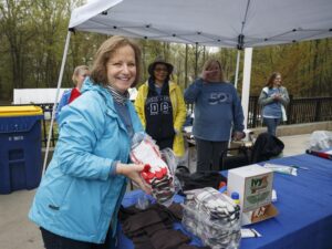 People at an outdoor event with a woman in a blue jacket holding a pack of gloves at a table under a canopy. Other participants, who live in apartments in DC, are in the background near a table with supplies. | DC Apartments by WC Smith