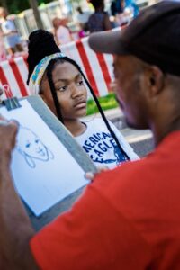 An artist sketches a portrait of a young person at an outdoor event with striped booths in the background, reminiscent of lively community gatherings near DC apartments. | DC Apartments by WC Smith