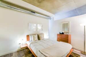 bedroom with bed, dresser and exposed concrete ceiling at the agora at the collective apartments in the capital riverfront washington dc