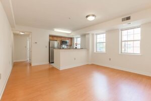 open layout of vacant apartment showing living area and kitchen with wood floors and large windows at the oaks apartments in washington dc
