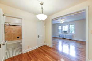 vacant room with wood floors, lighting and view of living area and bathroom at vacant sun room with exposed brick wall and large windows at 2629 39th Street apartments in washington dc
