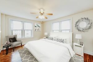 bedroom with bed, nightstands, sitting area, ceiling fan and large windows at hampton courts apartments in washington dc