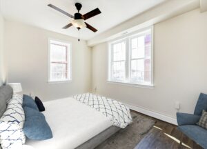 bedroom with bed, nightstand, sitting area, wood floors, ceiling fan and large windows at petworth station apartments in washington dc