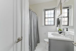 renovated bathroom with tub, toilet, vanity, large mirror and window at the dahlia apartments in washington dc