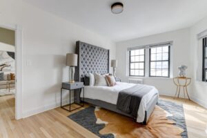 bedroom with bed, nightstand, large windows, wood floors and view of living area at the dahlia apartments in washington dc