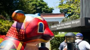 Colorful bear sculpture stands proudly in front of the Woodley Park-Zoo/Adams Morgan metro station entrance, with vibrant greenery providing a lush backdrop. | DC Apartments by WC Smith