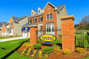 Brick entrance sign reading "Asheford" in front of suburban homes with manicured lawns and clear blue sky. | DC Apartments by WC Smith