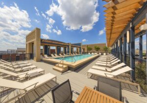 Rooftop pool area with lounge chairs and wooden pergola. Blue sky with scattered clouds in the background. | DC Apartments by WC Smith