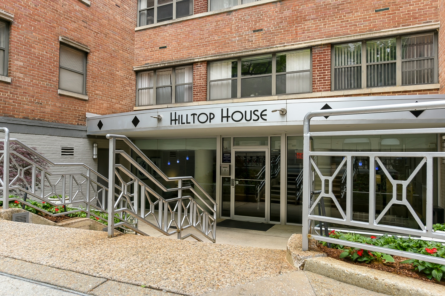 Entrance to Hilltop House, a brick apartment building with metal railings and steps leading up to elegant glass doors. | DC Apartments by WC Smith