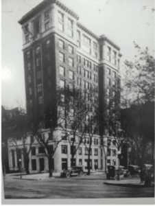 Historic black and white photo of a multi-story brick building with trees in the foreground and a vintage car parked on the street. | DC Apartments by WC Smith
