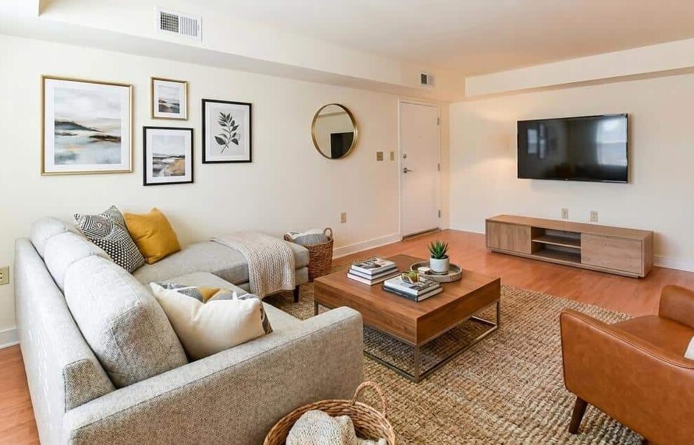 Modern Jasper Place living room with neutral decor, featuring two sofas, a wall-mounted TV, a wooden coffee table, framed artwork, and soft lighting. | DC Apartments by WC Smith