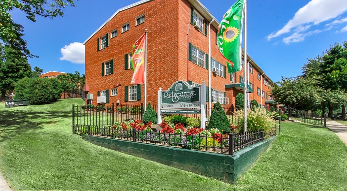 exterior of ridgecrest village, a brick apartment building with lush landscaping and welcome flags