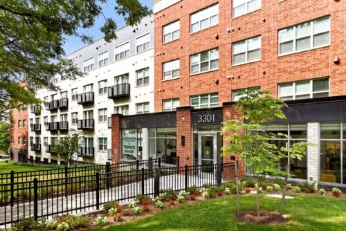 A modern apartment building, Terrace Manor features a red and white brick exterior, large windows, balconies, and a landscaped walkway leading to an entrance labeled "3301. | DC Apartments by WC Smith