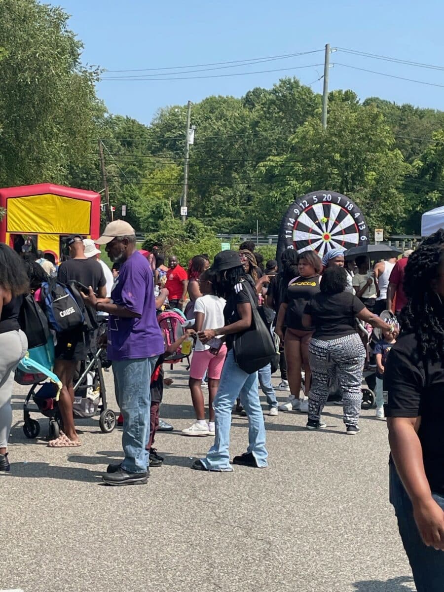 A diverse group of people, including DC Students, gathered outdoors at a vibrant back-to-school event. Strollers moved among the crowd while a dartboard backdrop provided fun under the trees in the background. | DC Apartments by WC Smith