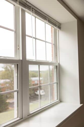 A view through a white-framed window with partially open blinds, showing a suburban area outside on an overcast day. | DC Apartments by WC Smith