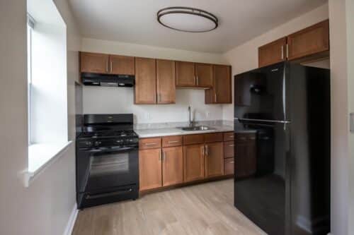 A kitchen with wooden cabinets, black appliances, a stove, refrigerator, and a sink. | DC Apartments by WC Smith