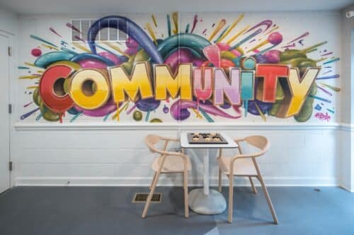 Colorful graffiti on a wall spells "COMMUNITY" above a small table with a chessboard and two chairs. | DC Apartments by WC Smith