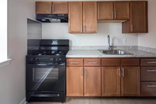 A kitchen with brown cabinets, a stainless steel sink, and a black gas stove. | DC Apartments by WC Smith