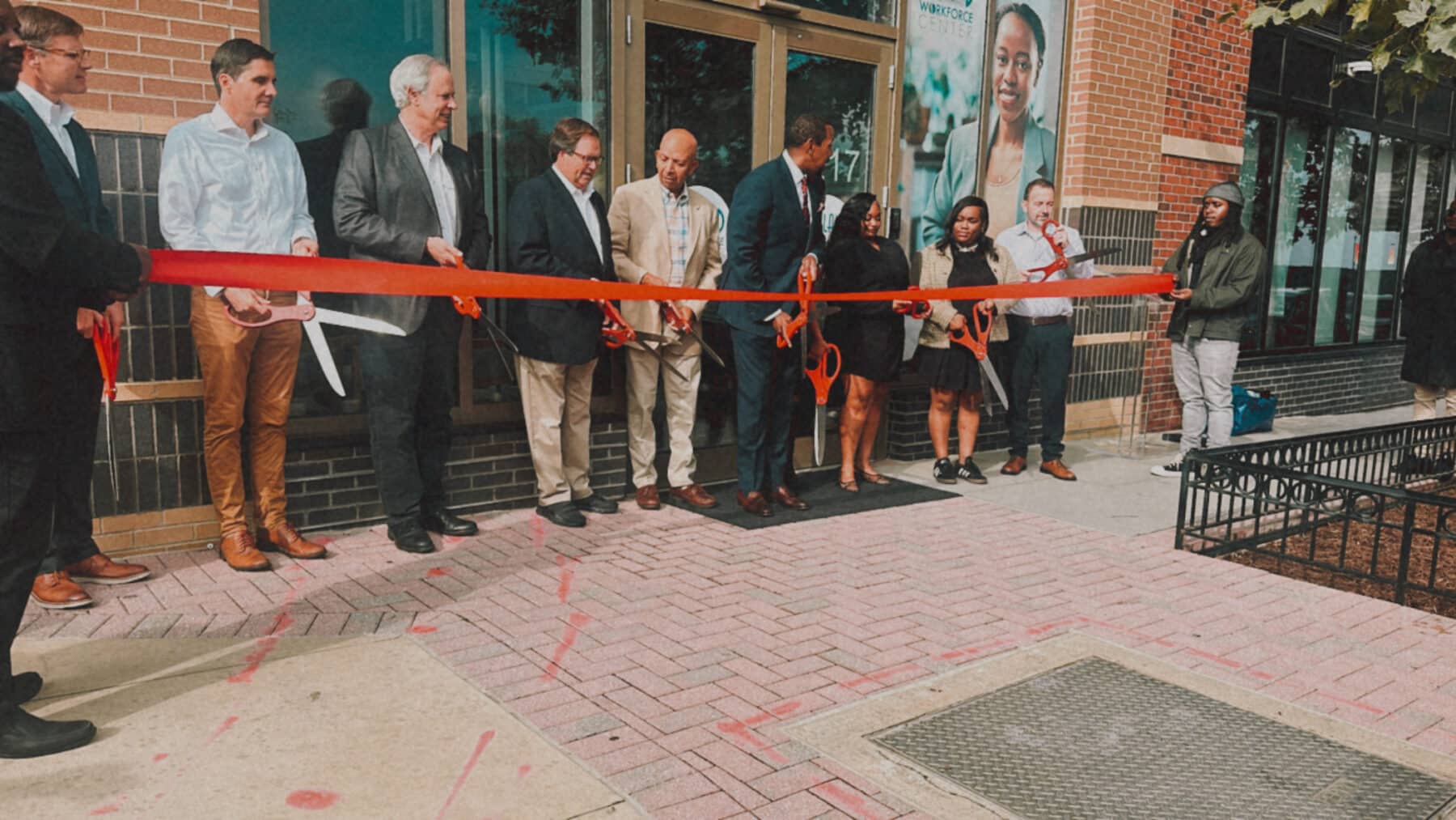 A group of people stand in front of the Skyland Workforce Center, cutting a large red ribbon during its 10th Anniversary ribbon-cutting ceremony. | DC Apartments by WC Smith