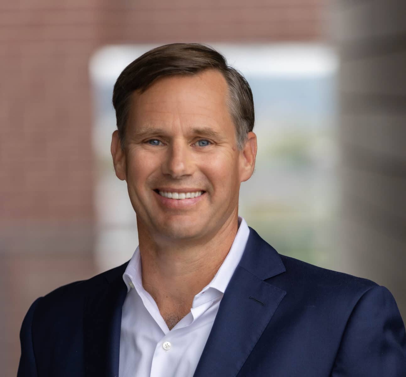 Brad Fennell, dressed in a blue suit and white shirt, smiles confidently at the camera in an outdoor setting. | DC Apartments by WC Smith